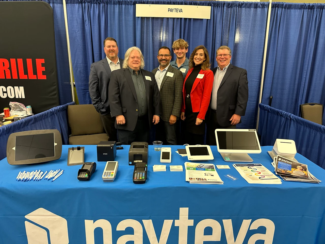 Six Payteva representatives behind a trade show booth displaying payment processing equipment